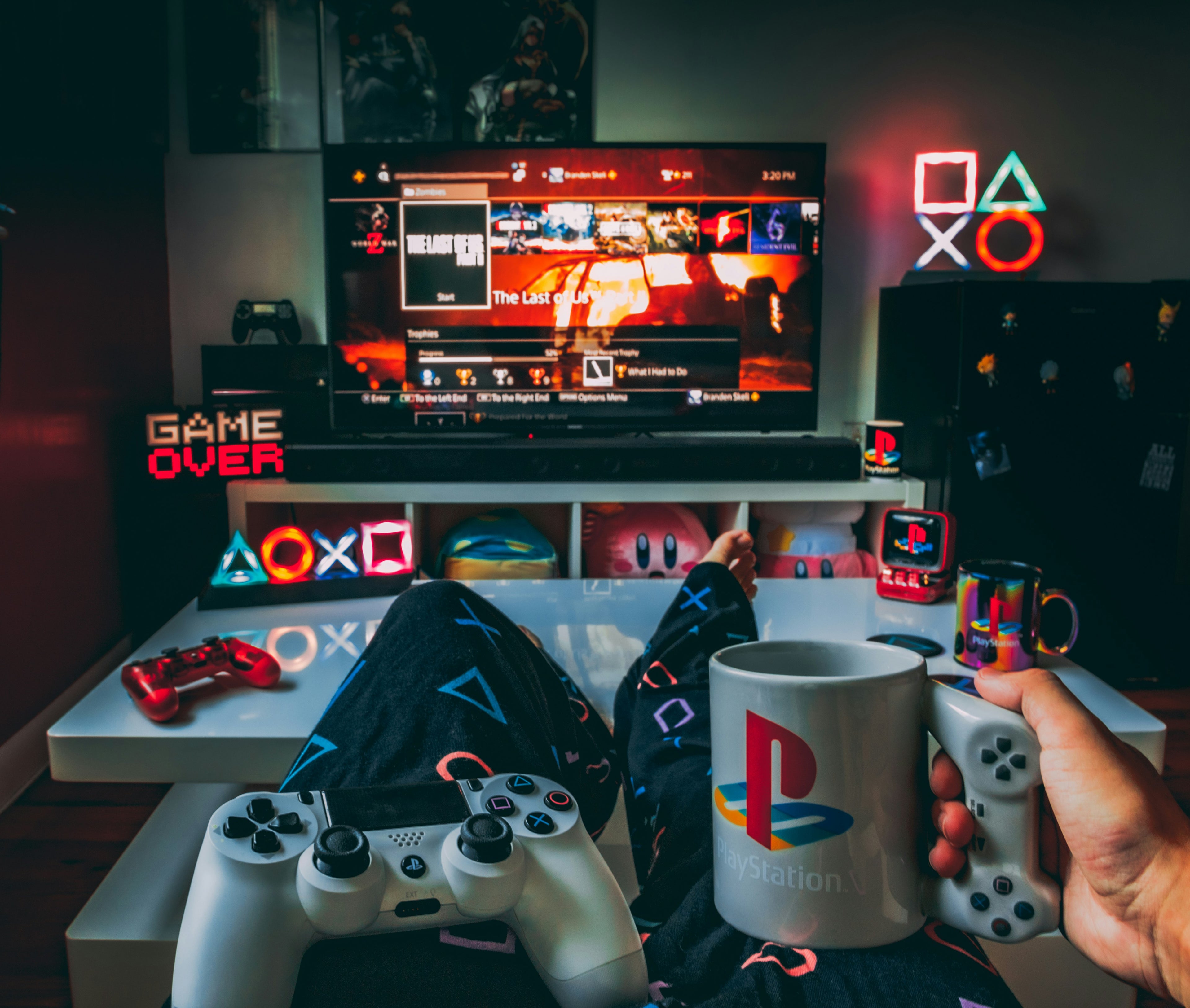 Person holding a PlayStation mug with gaming setup and TV in the background